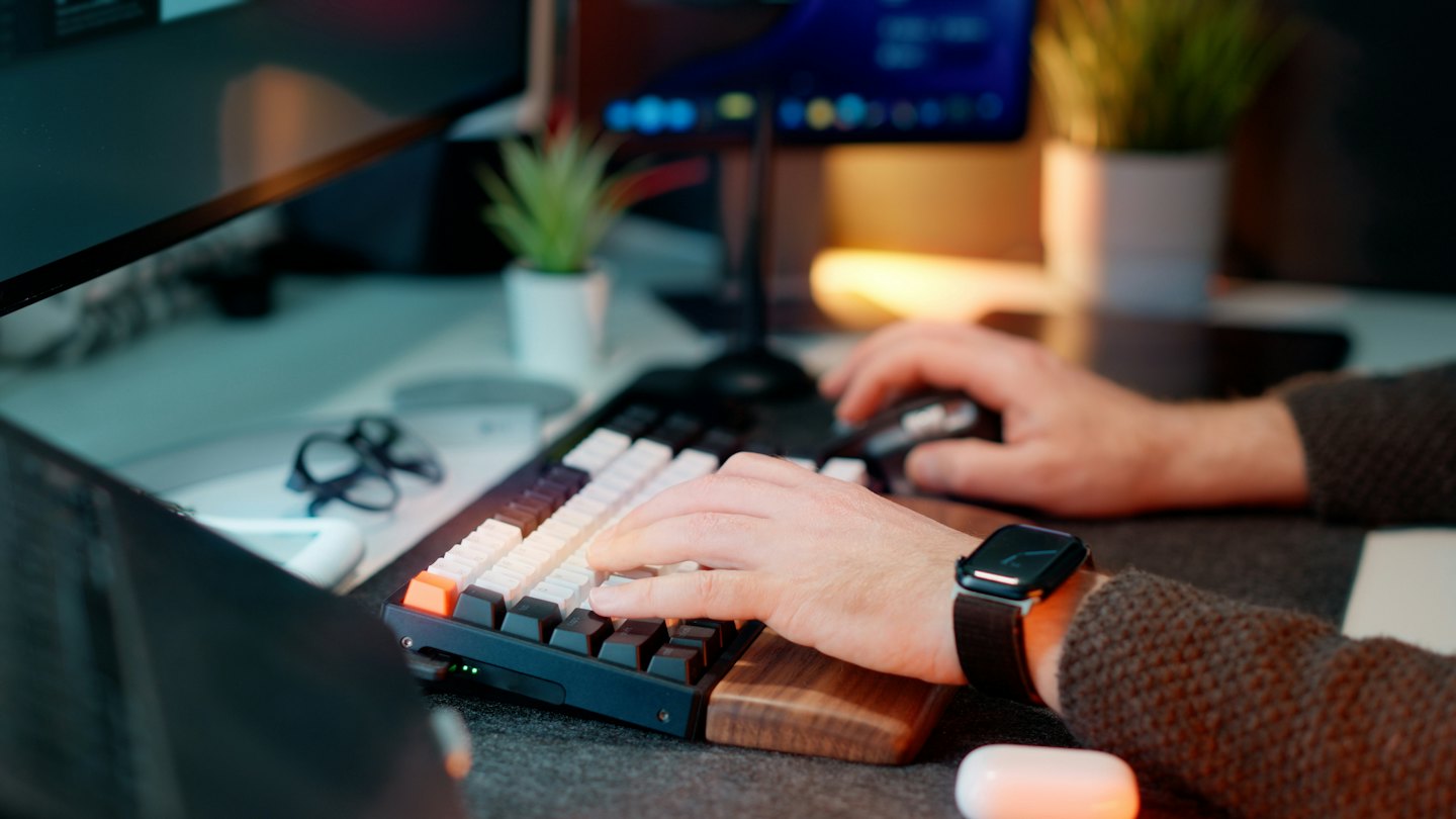 Hands typing on a mechanical keyboard at a wooden desk.